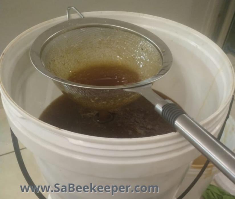 honey being sieved once it is harvested in a bucket. to collect pieces of wax
